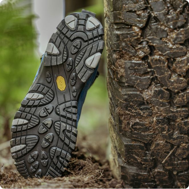 Merrell boot leaned up against a Jeep tire, showing the great traction of both.