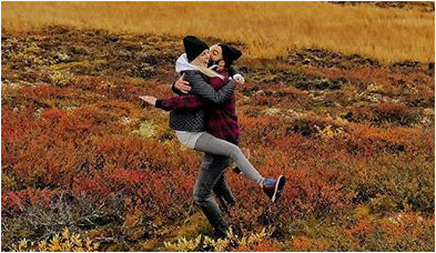 Andrew and Adrienne McDermott hugging joyously on a beautiful fall day in a field.
