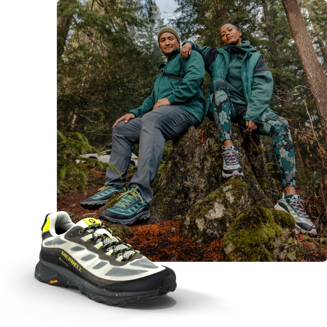 People wearing boots while sitting on a large rock in a forest.