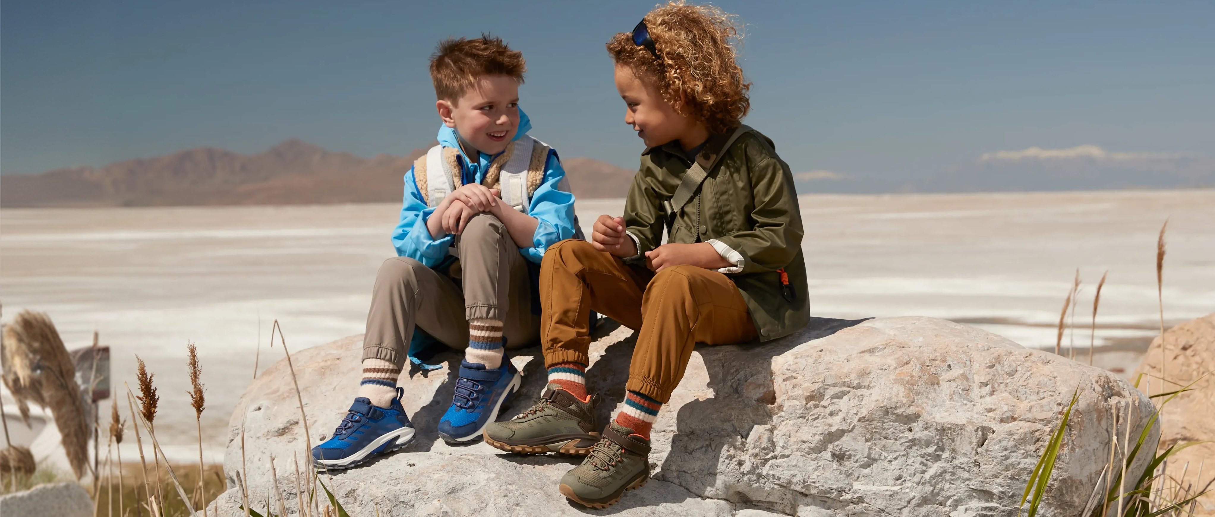 Two kids sitting on a rock wearing Merrell shoes