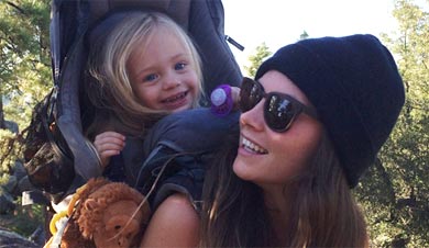Morgan Brechler smiling at her young daughter on her back as her young daughter smiles back excited for their next hike.