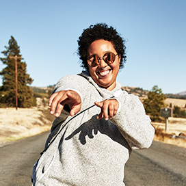 A super-happy person wearing mirrored shades stands on a sunny highway giving us double finger guns.