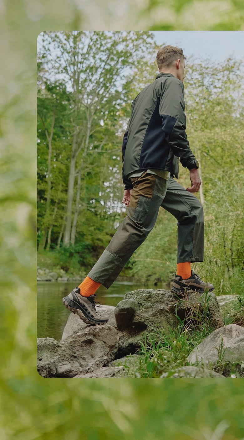 Person hiking outside near a creek wearing Merrell shoes