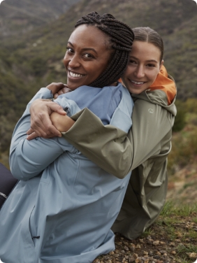2 people sitting outside in mountains, hugging while wearing Merrell gear.