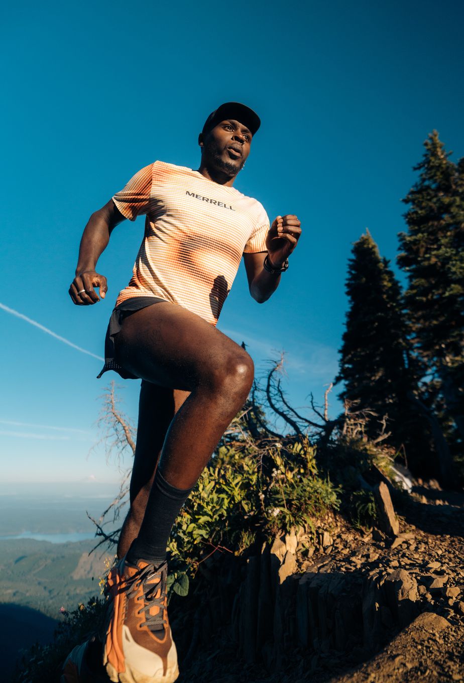 Coree Woltering running uphill on a mountain trail beneath a blue sky.