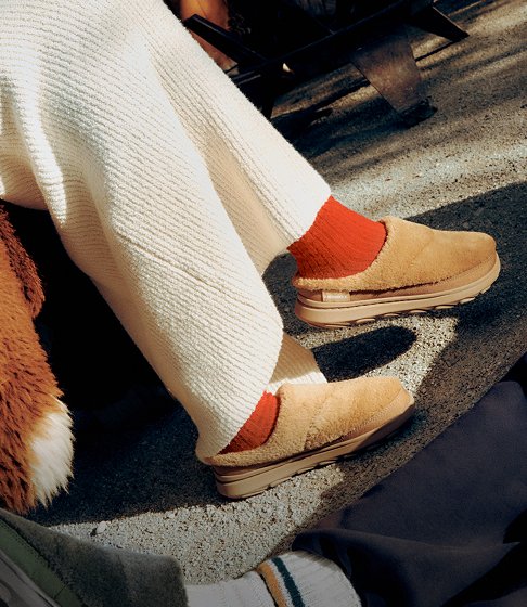 Person in tan Merrell winter boots sitting in a deck chair in the snow above a mountain lake.