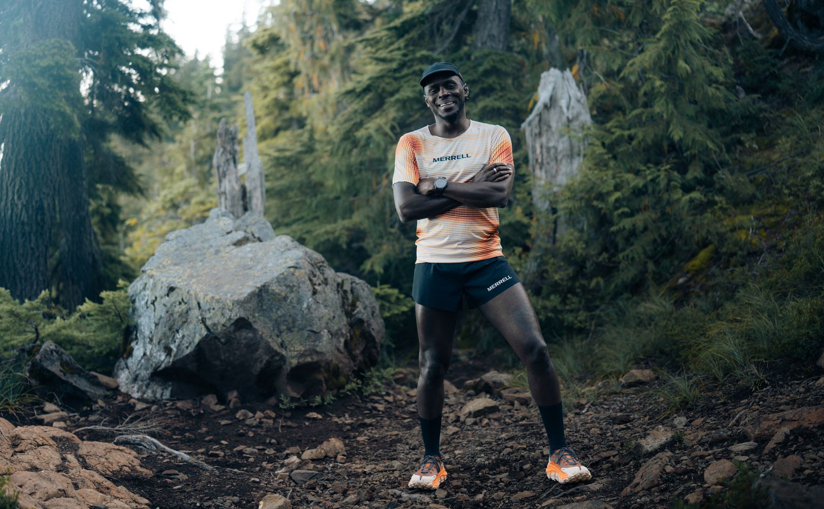 Coree Woltering standing on a rocky forest trail in Merrell running gear.