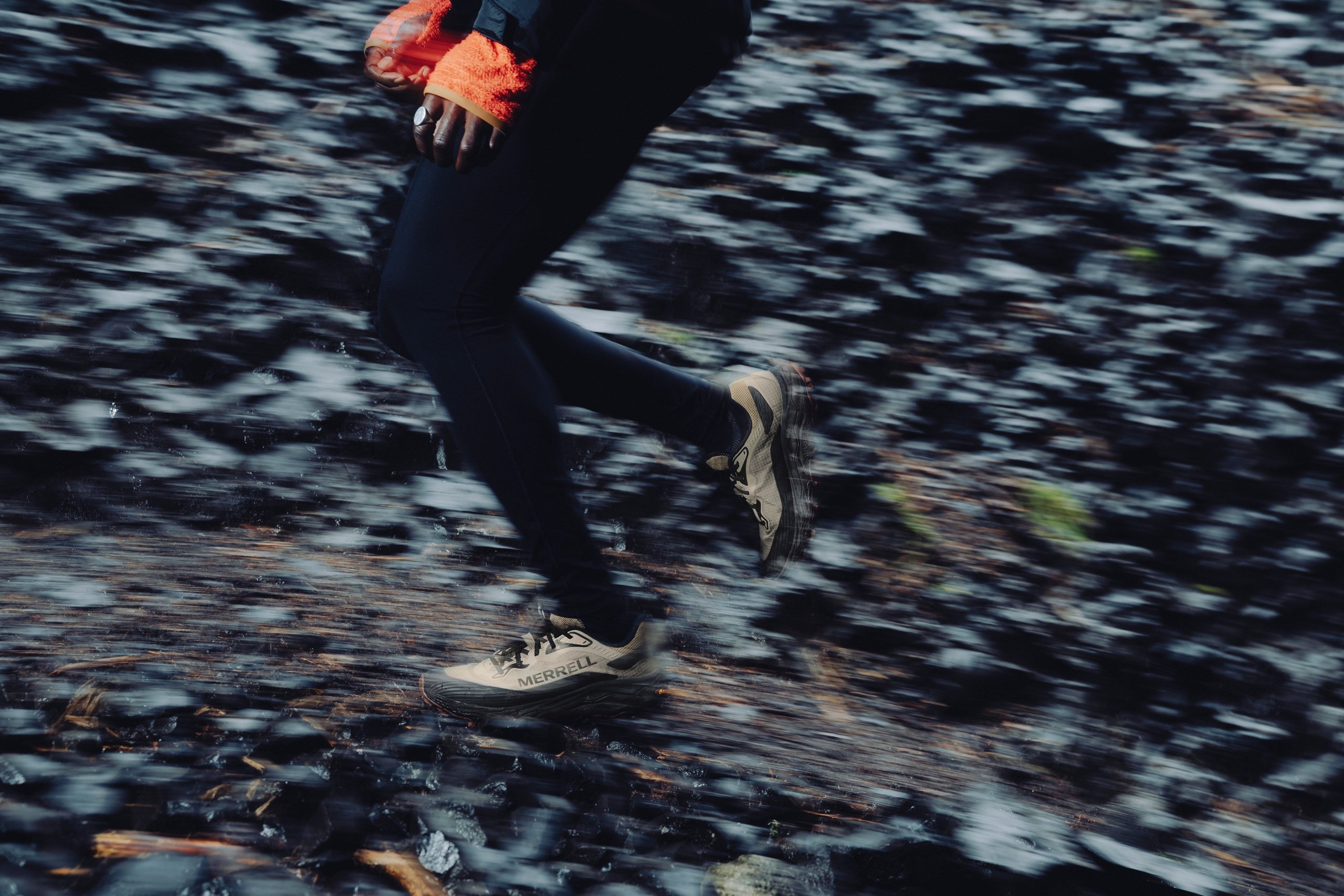 Trail runner in Merrell shoes sprinting over wet, rocky terrain