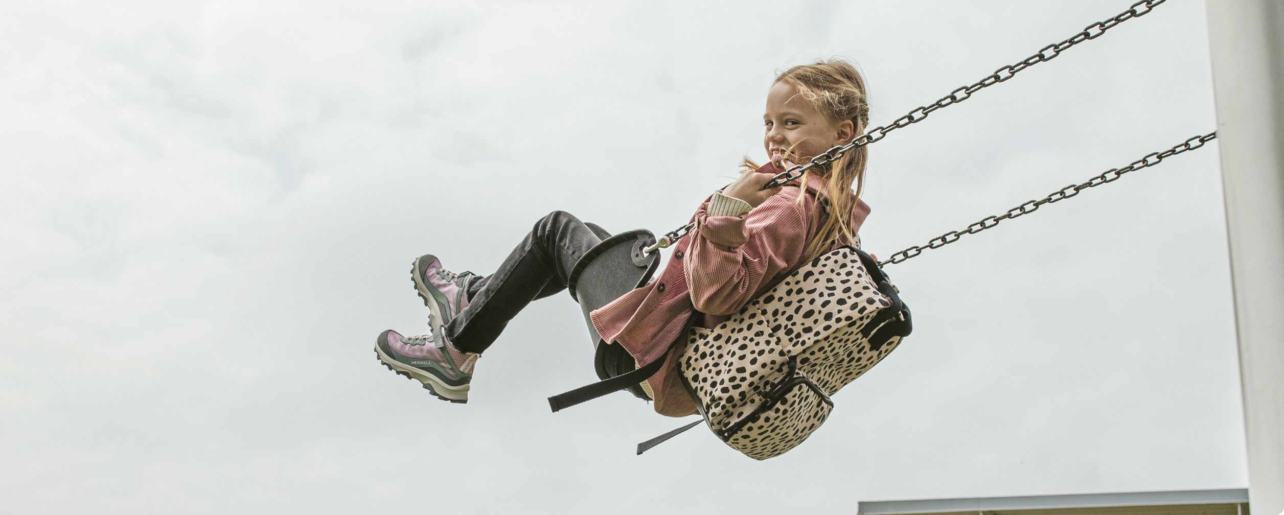 Little kid having fun playing on a swing wearing a backpack.