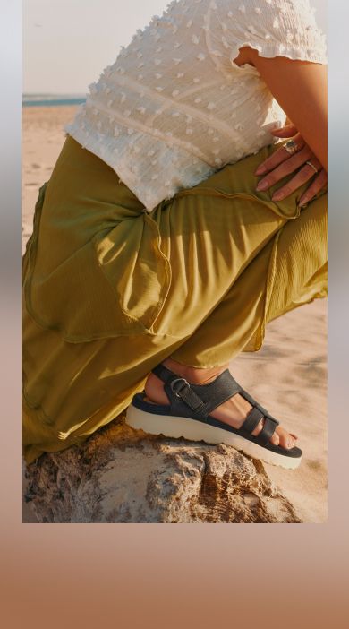 Person sitting on a rock at the beach wearing Merrell sandals