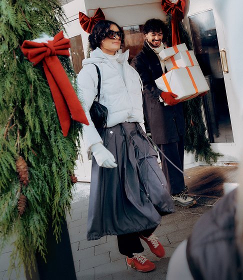 Person in red Merrell shoes holding a wrapped gift beside a stack of presents.