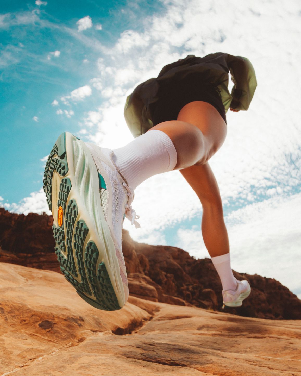 A trail runner jumping across red rock beneath a blue sky.