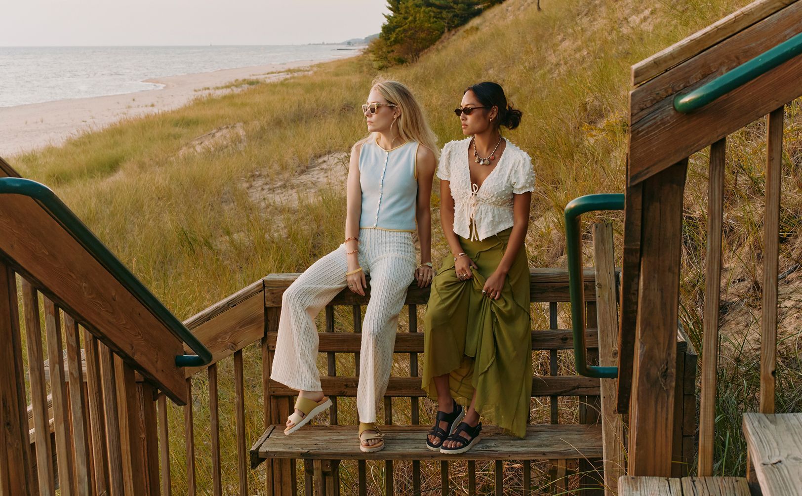 Two women sitting together on stairs looking out over the beach.