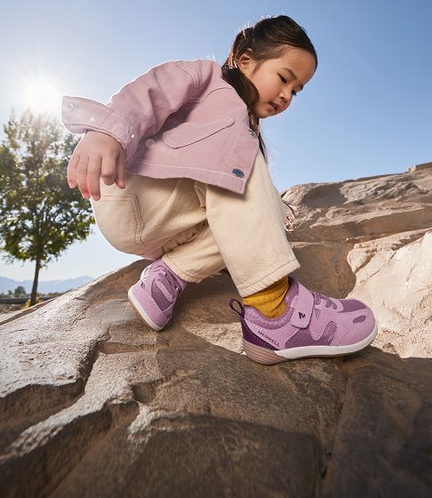 Child crouching on a rock outdoors.
