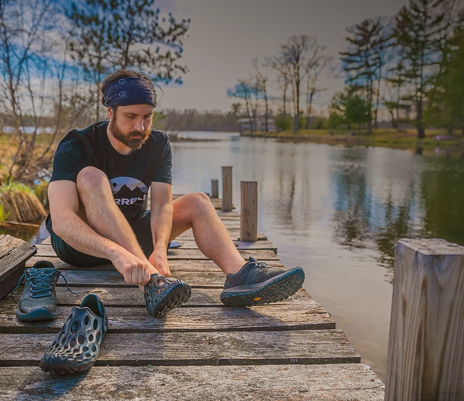 Man on a dock, switching shoes.