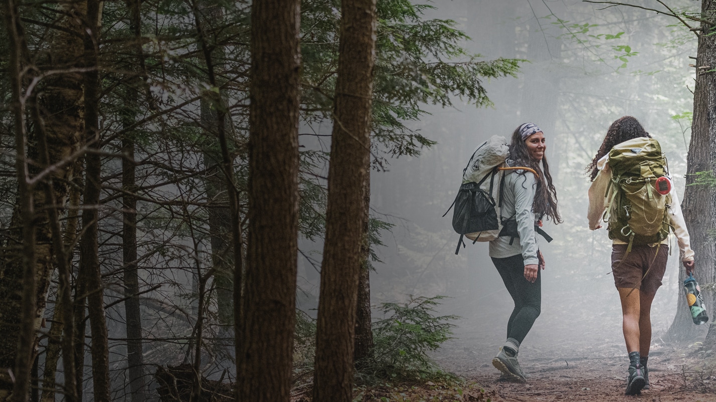 Two women backpacking in a foggy woods, wearing Merrell Bravada hiking shoes