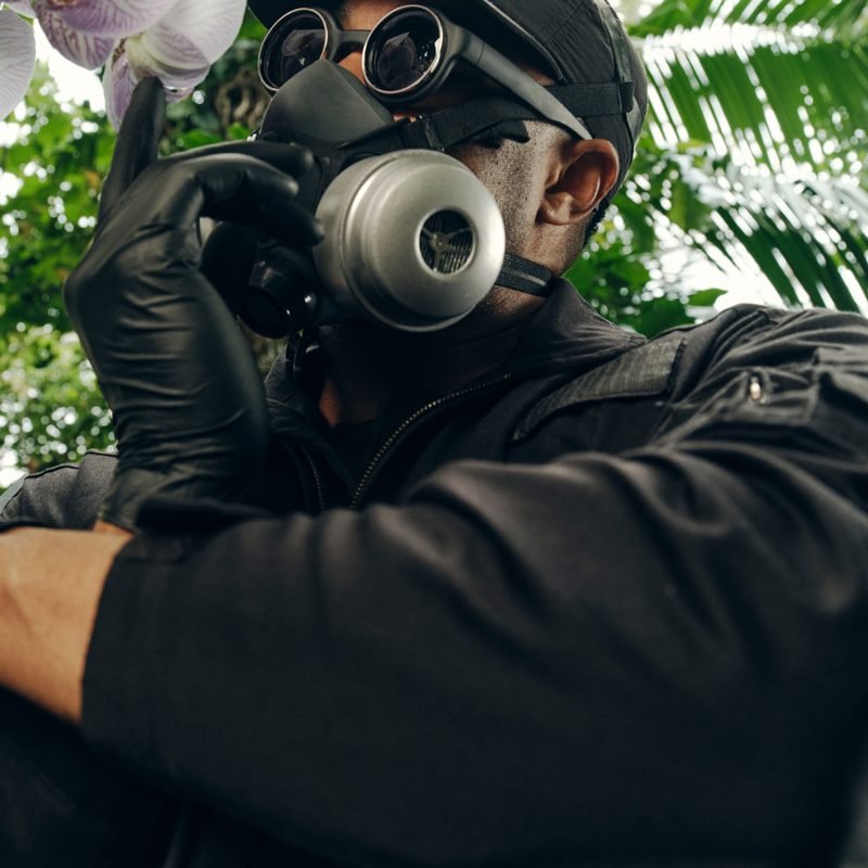 Mr. Flower Fantastic in a gas mask holding an orchid bloom