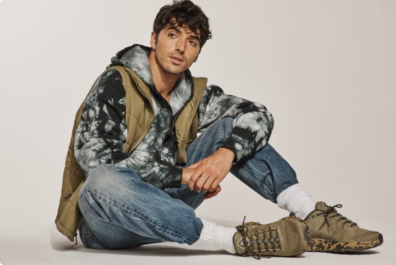 Taylor Zakhar Perez sitting on the ground with a white background wearing Merrell gear.