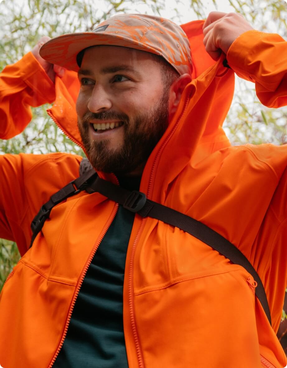 Person wearing orange rain jacket, pulling hood over head