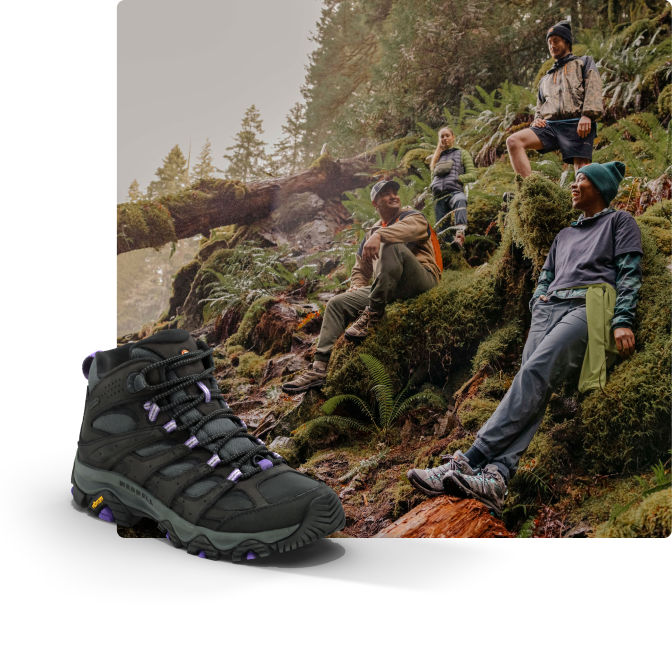 People wearing boots while sitting on mossy outcrop on the side of a mountain.