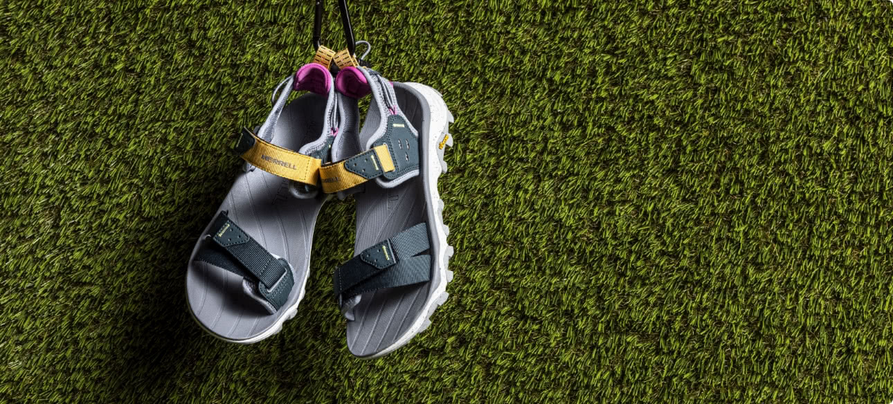 A pair of Merrell sandals hanging on a grass wall.