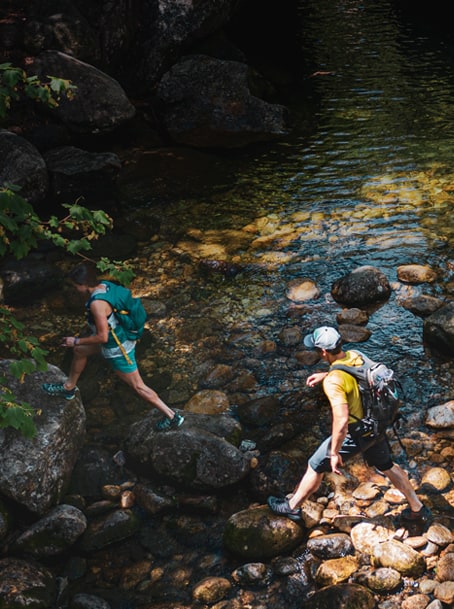 Two people out for a hike, crossing a creek.
