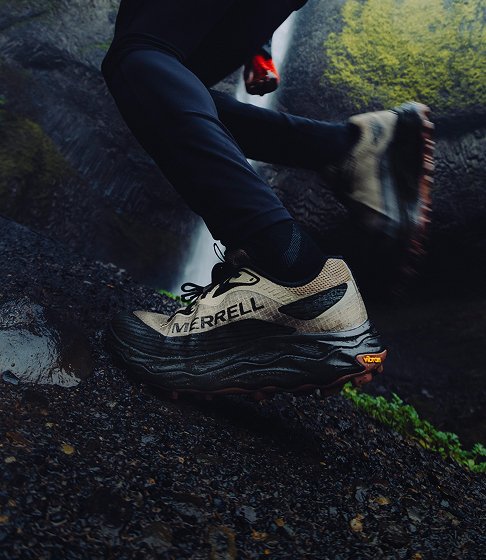 Close-up of Merrell trail shoes climbing a wet, mossy rock.