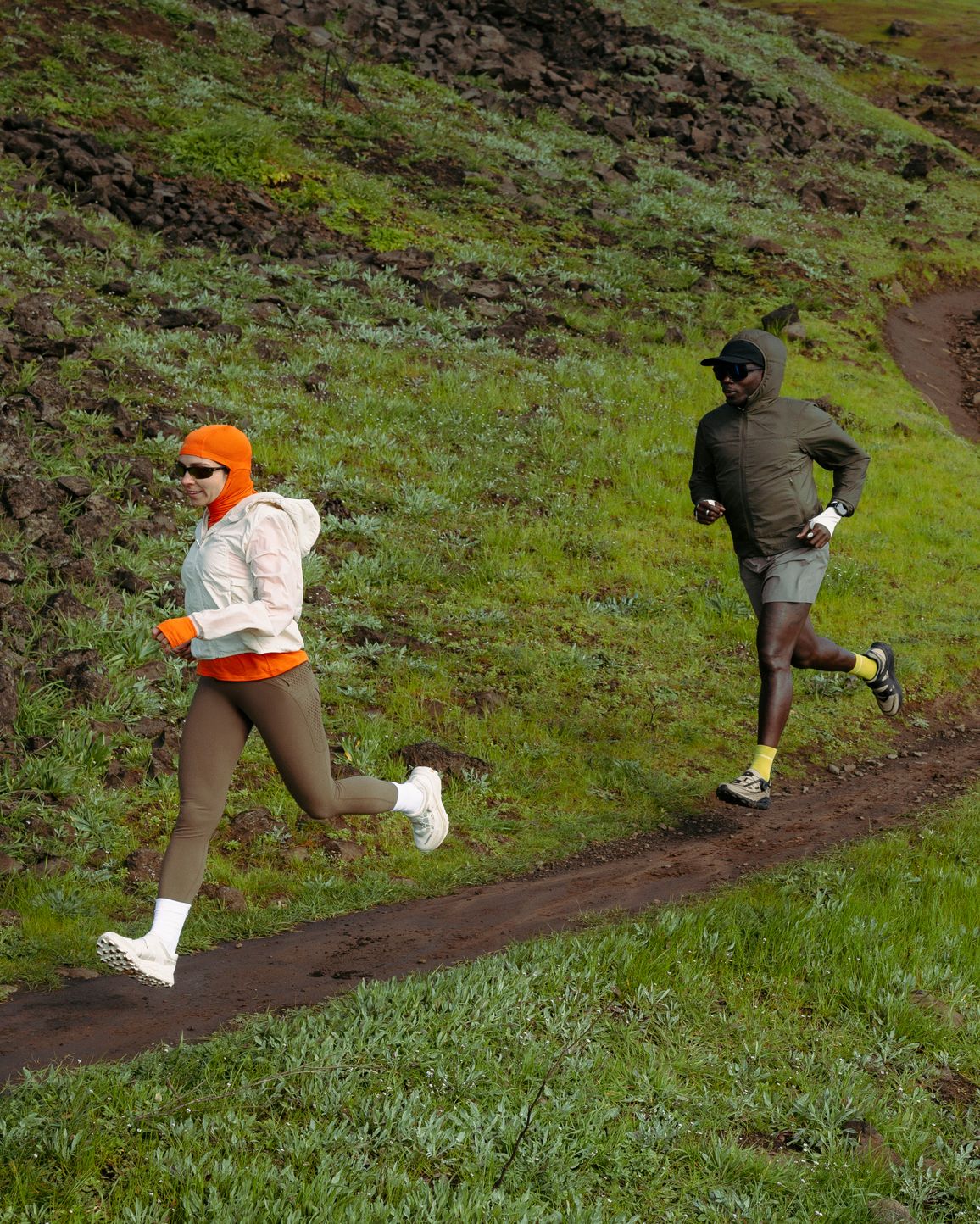 Two trail runners following a winding path across a green hillside.