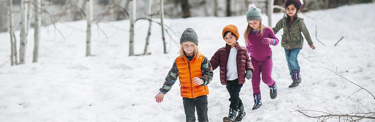 Kids walking in a line through the snow enjoying themselves outdoors.