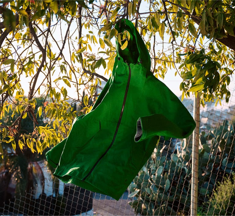 Green whisper rain jacket hanging from a fence.
