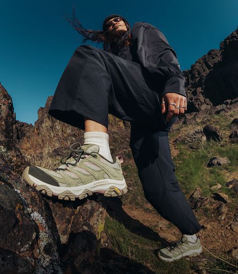 Person seated on rocks in Merrell shoes.