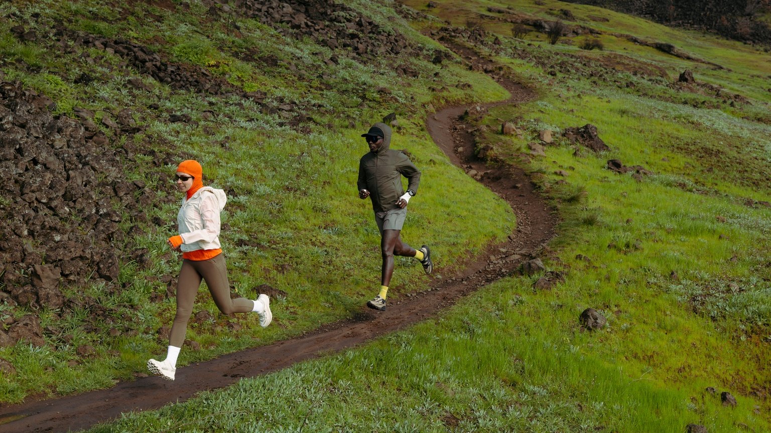 Two trail runners on a winding path through green hills