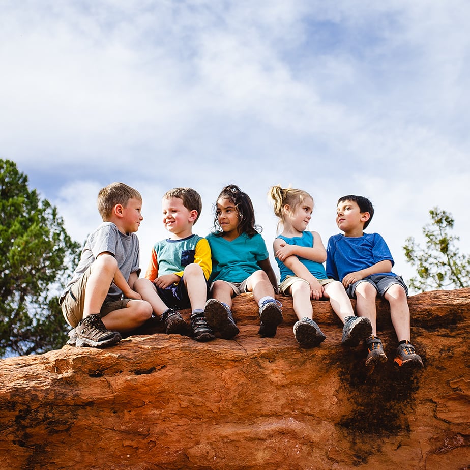 5 kids taking a rest on a rock during a hike