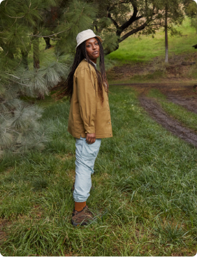 Woman standing in front of a trail and tree with a cabin in the background